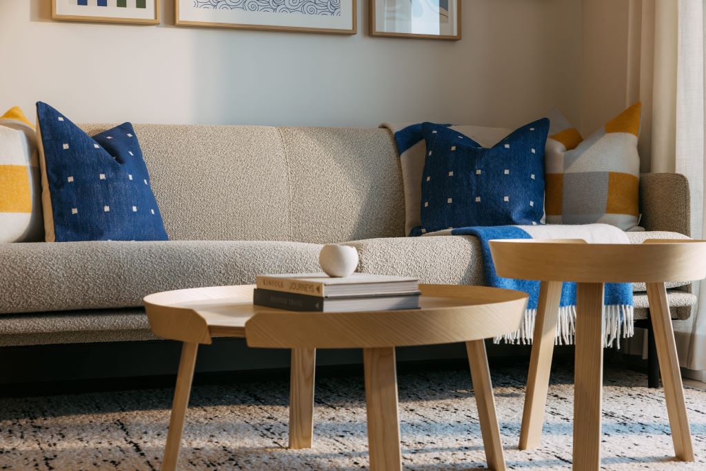 Stylish living room with beige sofa, blue pillows, wooden coffee tables, and cozy decor. Modern interior design.