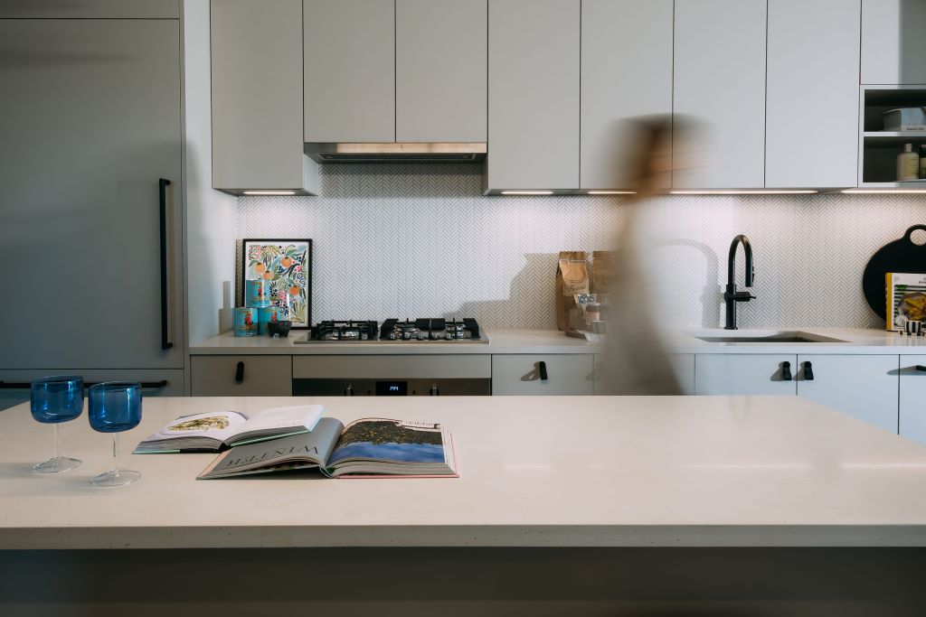 Modern kitchen with sleek white cabinets, open book, blue glasses, and blurred motion of person.