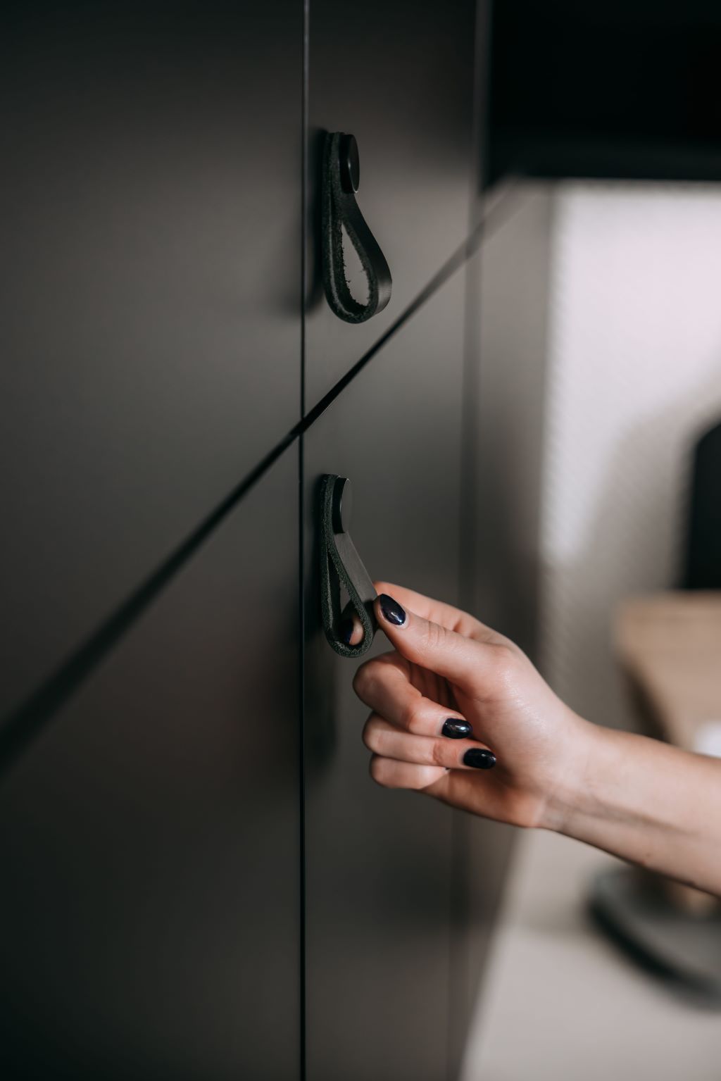 Hand opening a sleek black cabinet with leather loop handle, highlighting modern kitchen storage design.
