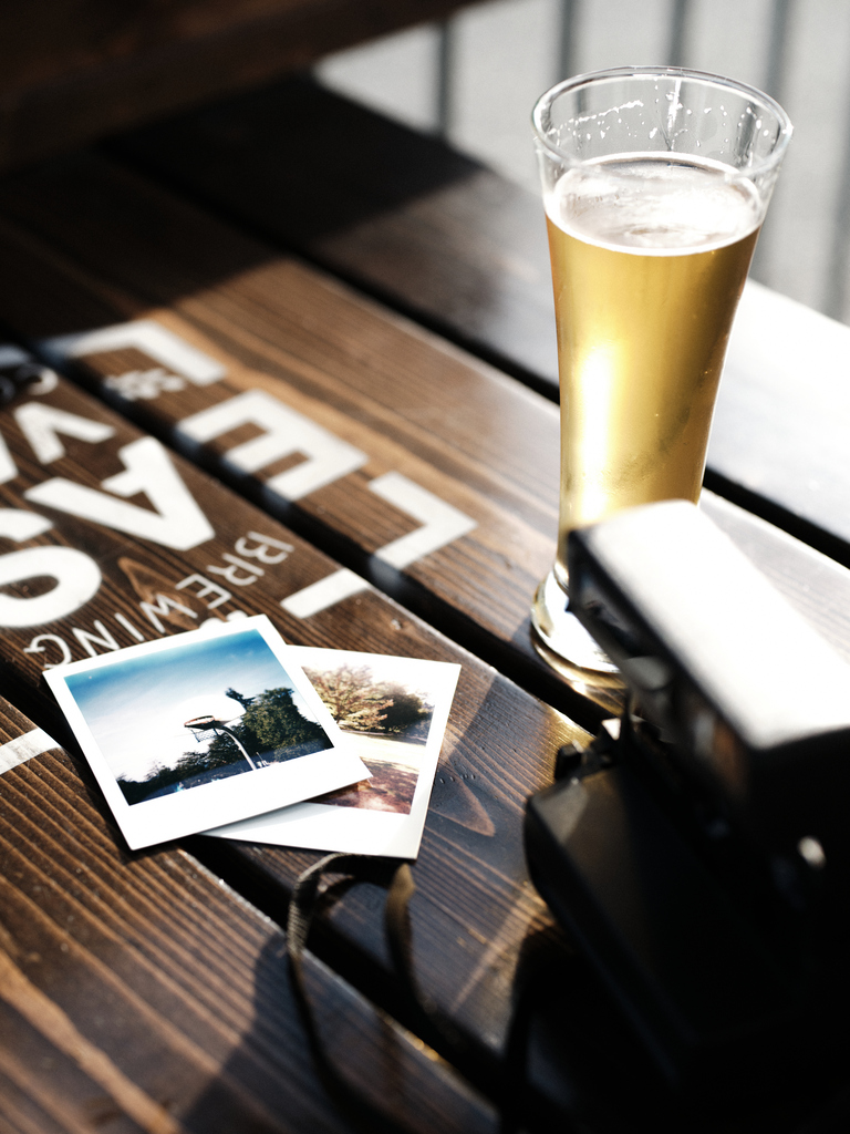Cold beer in a glass on a wooden table with vintage photos and a camera, capturing moments of travel and nostalgia.