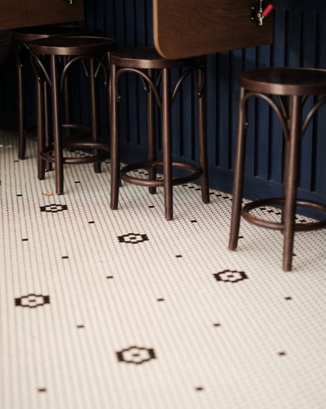 Bar stools with elegant wooden design against a blue wall, on a vintage tiled floor with geometric patterns.