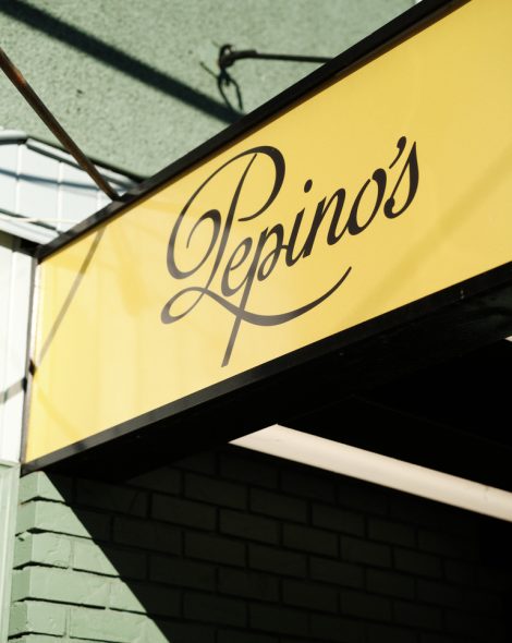 Yellow sign with elegant black script reading Pepino's above a green brick wall.